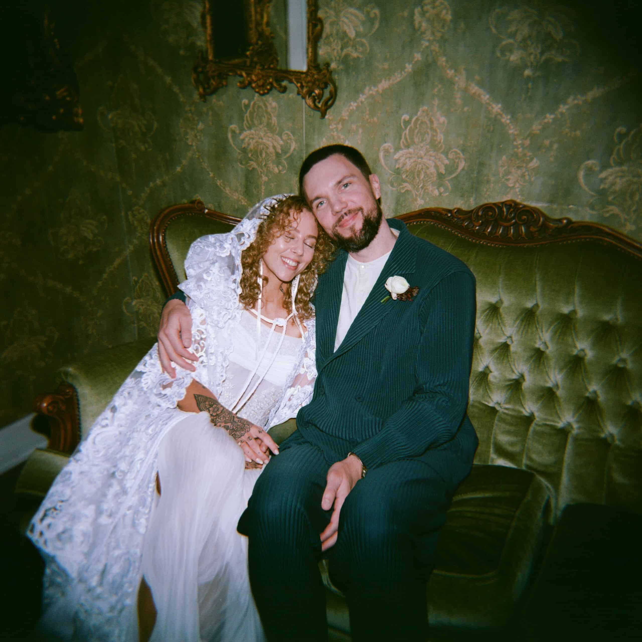 Bride and groom sitting on vintage green sofa at wedding reception.